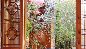Un couloir en bois, surmonté d’une arche faite de plantes en bambou et agrémenté d’une porte traditionnelle.