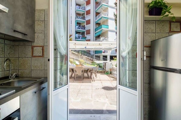 Une cuisine moderne dotée d’un four encastré, d’un réfrigérateur en acier inoxydable et d’une fenêtre donnant sur un balcon aménagé avec une table et des chaises.