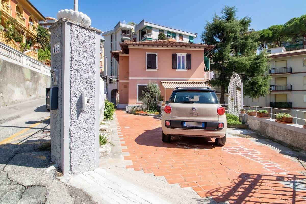 A beige car parked on a brick pathway in front of a two-story building with a balcony.
