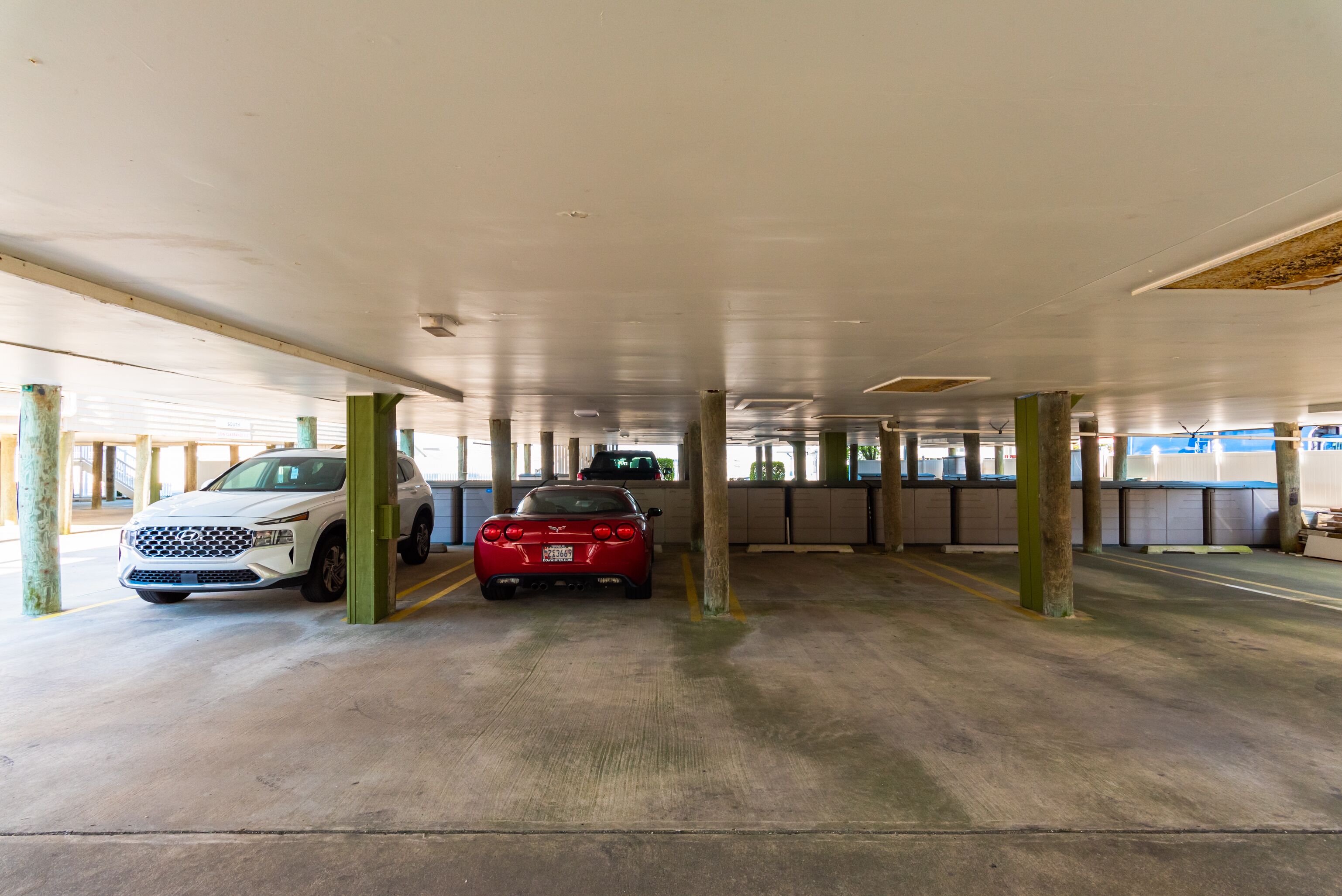 Een parkeergarage met twee geparkeerde auto's, betonnen pilaren en een vlakke betonvloer.