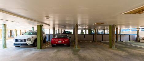 Een parkeergarage met twee geparkeerde auto's, betonnen pilaren en een vlakke betonvloer.