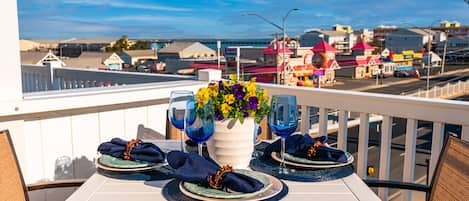 A balcony table set with blue napkins, a vase of flowers, and wine glasses.