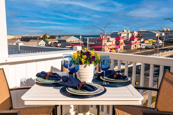 A balcony table set with blue napkins, a vase of flowers, and wine glasses.