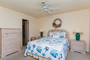A bedroom with a bed, dresser, nightstands, lamps, and a ceiling fan.
