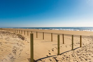 A sandy beach with wooden posts and footprints, leading to the ocean.