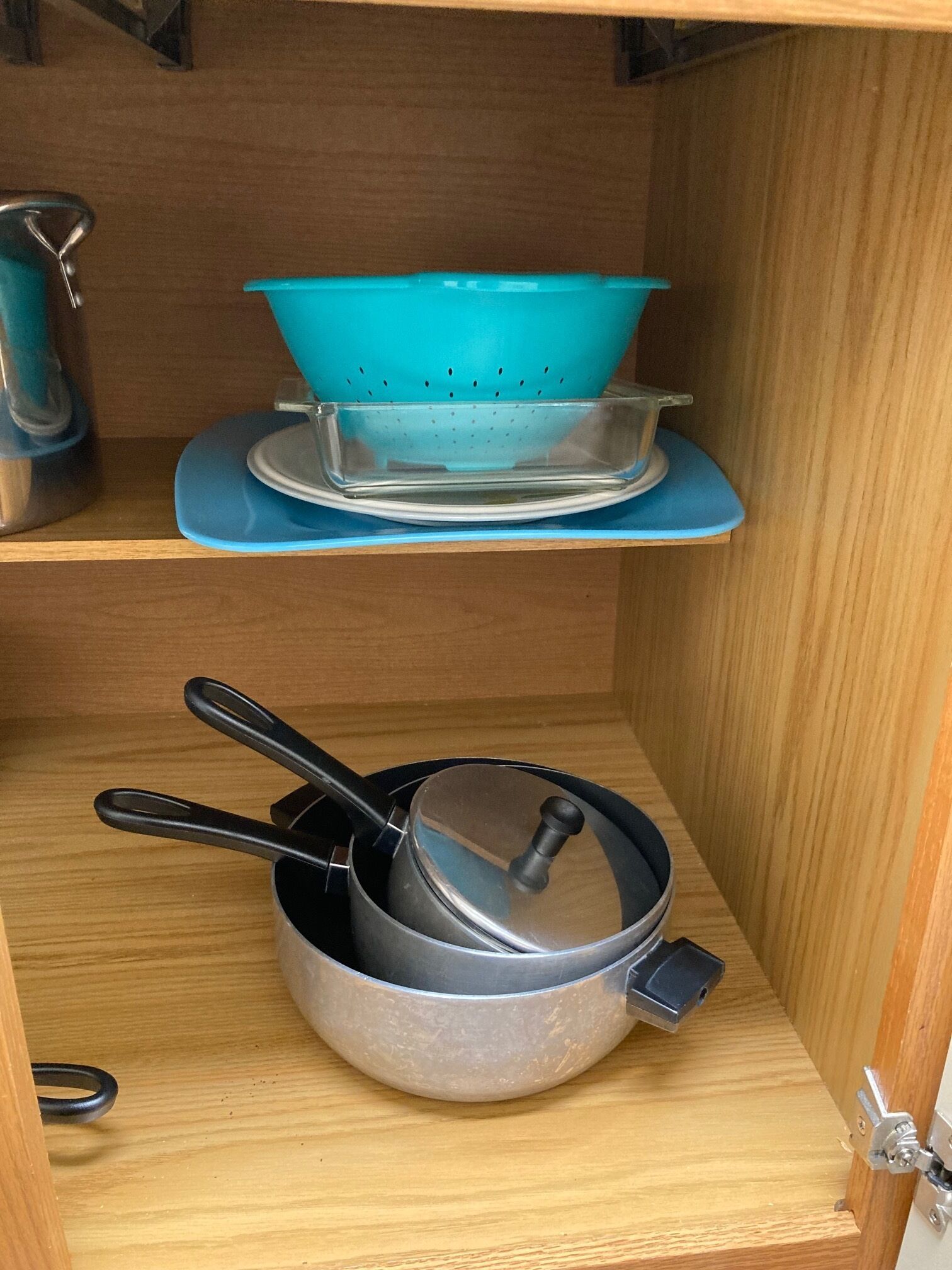 Ein Küchenschrank mit einem blauen Sieb auf einer blauen Serviertablett, einem Topf mit Deckel und einem Wasserkocher.