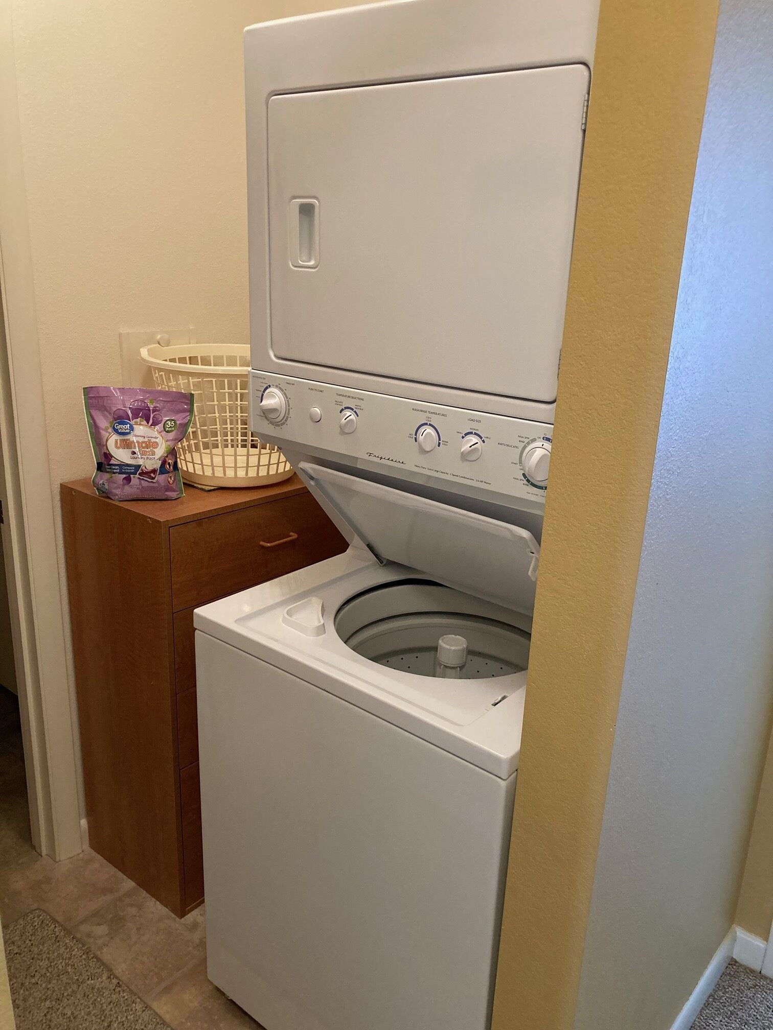 Un appareil combiné lave-linge et sèche-linge à chargement frontal, doté d’un panneau de commande, d’un panier à linge et d’un sac de lessive.