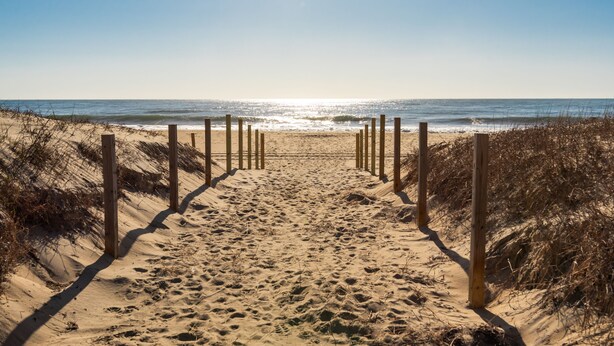 Ein Sandweg am Strand, der zum Meer führt, mit Holzbalken an beiden Seiten.