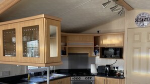 A compact RV kitchen with wooden cabinets, a stove, microwave, and a sink. - Immaculate 2-bed Static Caravan at Monrieth (Newton Stewart)