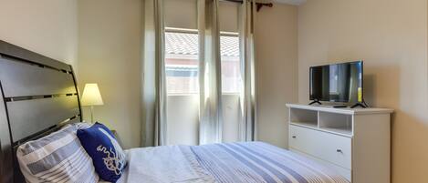 A bedroom with a bed, a TV on a white dresser, a lamp, and a window with curtains.