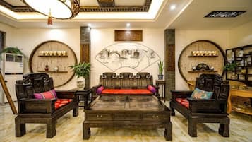 A traditional room with a central sofa set, a coffee table, and two armchairs. There are decorative wall panels and a ceiling light fixture.