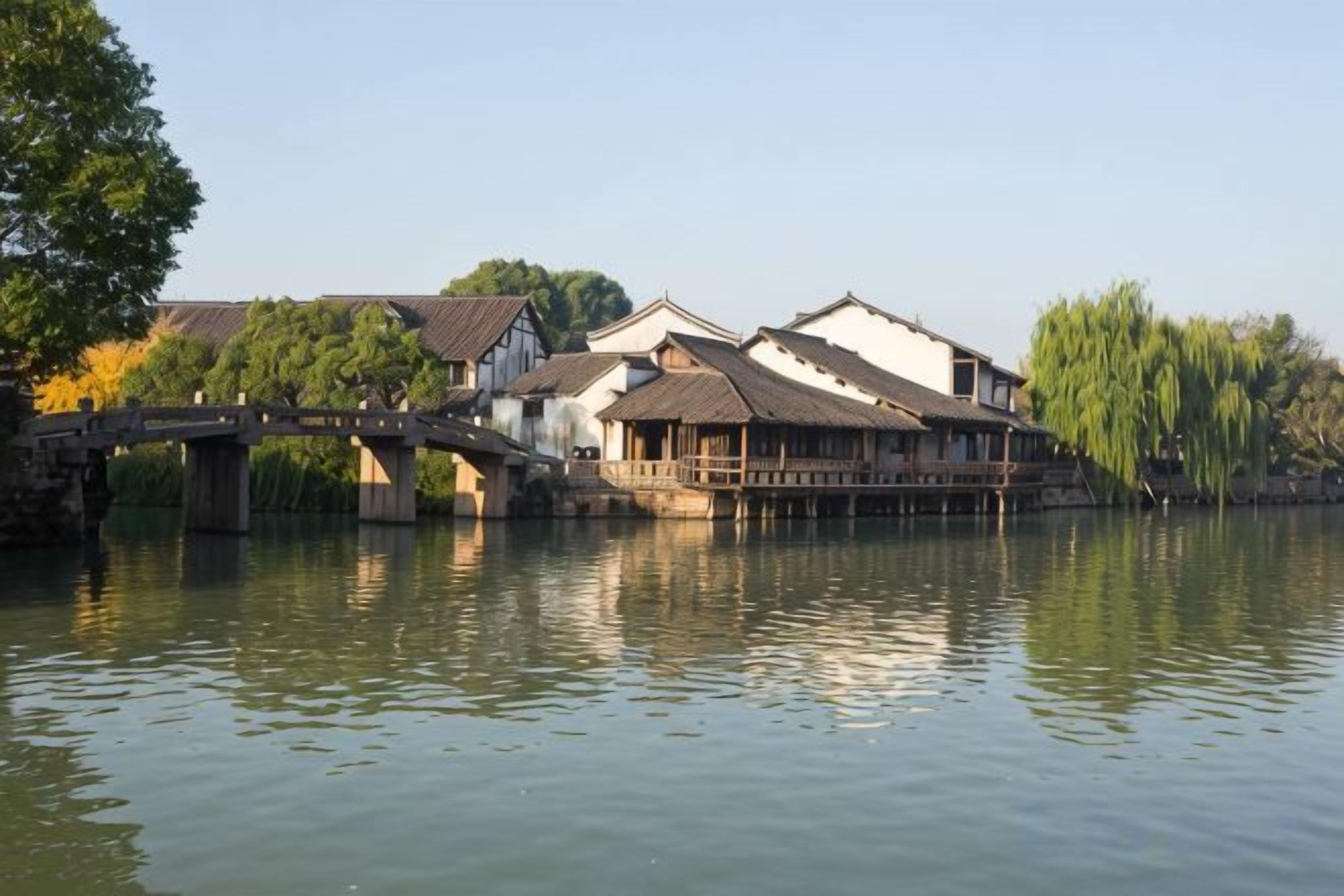 A traditional building with a bridge over water, reflecting the structure and trees.