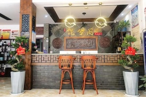 Un área de recepción con mostrador, dos taburetes de bar, plantas decorativas y una pantalla montada en la pared.