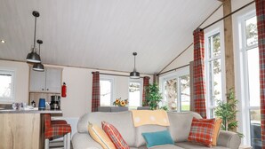 A cozy living room with a sofa, a small table, and a kitchen area with a counter and cabinets. - Piran Lodge (Padstow)