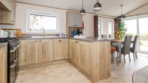 A modern kitchen with wooden cabinets, a central island, and pendant lighting. - Piran Lodge (Padstow)