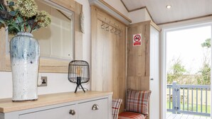 A bathroom with a wooden vanity, a vase with flowers, a hanging light fixture, and a bench with a plaid cushion. - Piran Lodge (Padstow)
