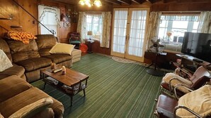 A cozy cabin interior with a wooden ceiling, a green striped carpet, a sofa, a coffee table, and a television. - Clearview Limit 6 4 Bedroom Villa by RedAwning (Sebago)