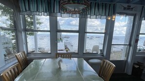 A dining area with a large table and chairs, large windows with a view of the sea, and a ceiling fan. - Clearview Limit 6 4 Bedroom Villa by RedAwning (Sebago)
