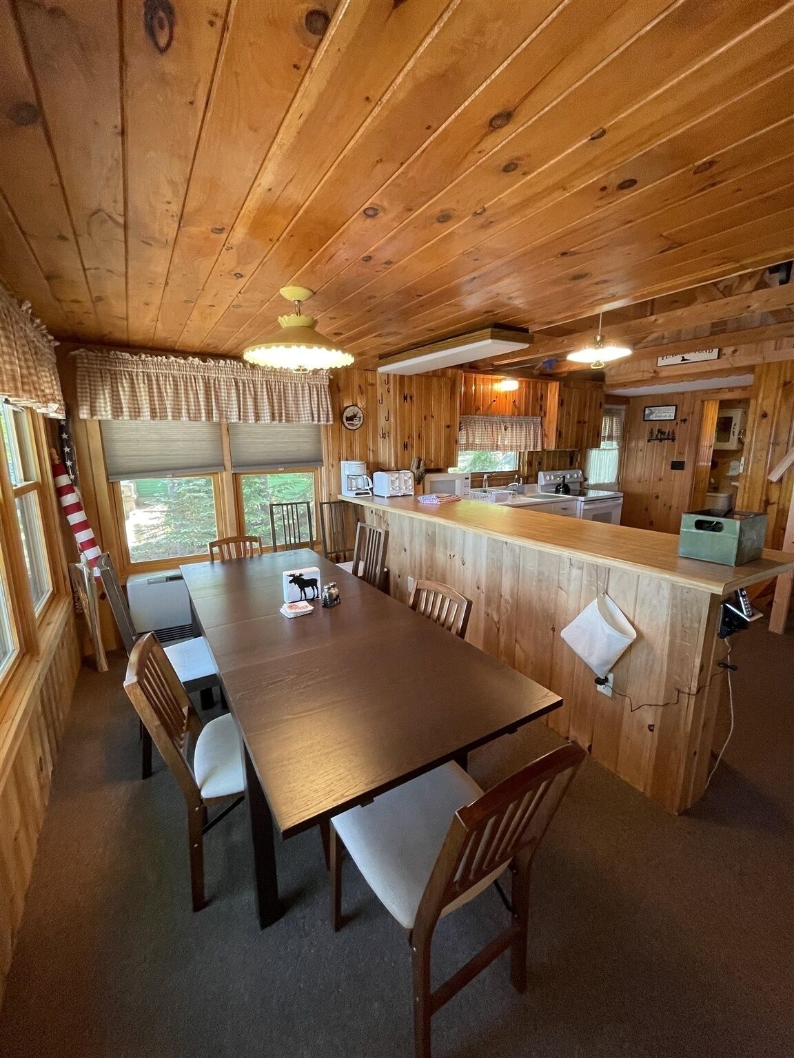 A wooden cabin interior with a dining table, chairs, a kitchen area, and a bar counter.
