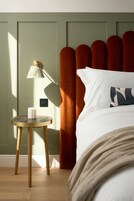 A neatly arranged bedroom with a bed, a bedside table with a lamp, and a power outlet on the wall.