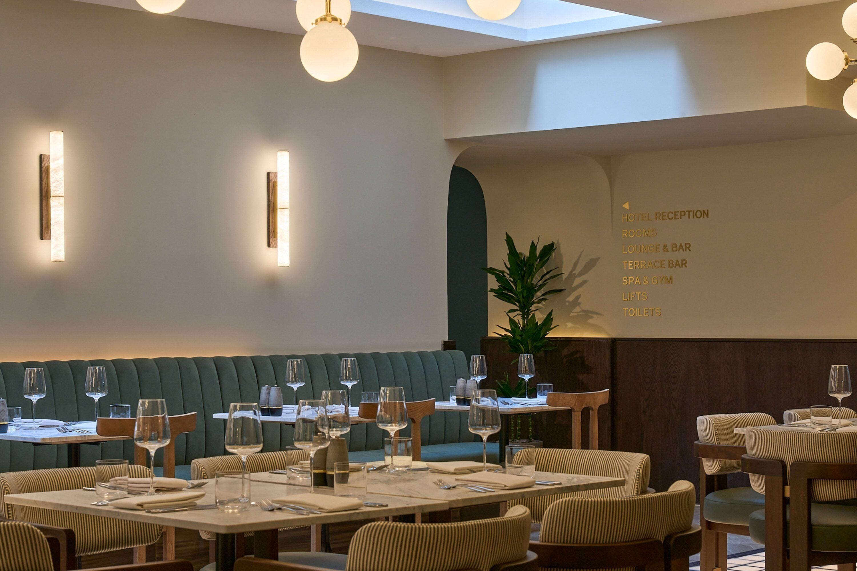 Un restaurante con una zona de asientos en cabinas verdes, mesas con sillas y una pizarra de menú que enumera los servicios del hotel.