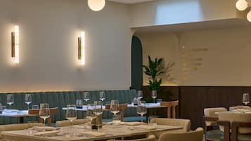 Un restaurante con una zona de asientos en cabinas verdes, mesas con sillas y una pizarra de menú que enumera los servicios del hotel.