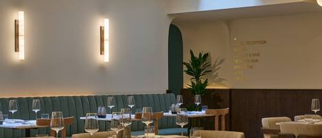 A restaurant with a green booth seating area, tables with chairs, and a menu board listing hotel amenities.