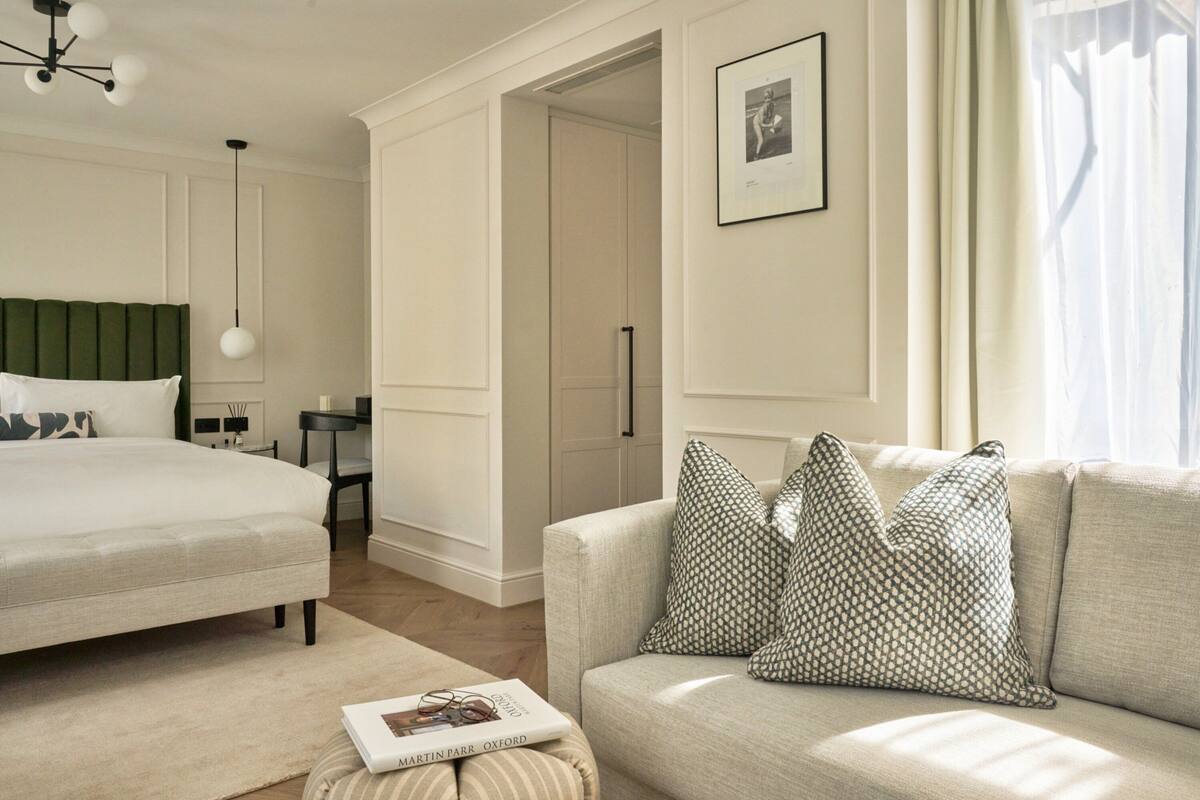 A bedroom with a bed, a sofa, a reading chair, a bedside table, a lamp, and a framed picture on the wall.