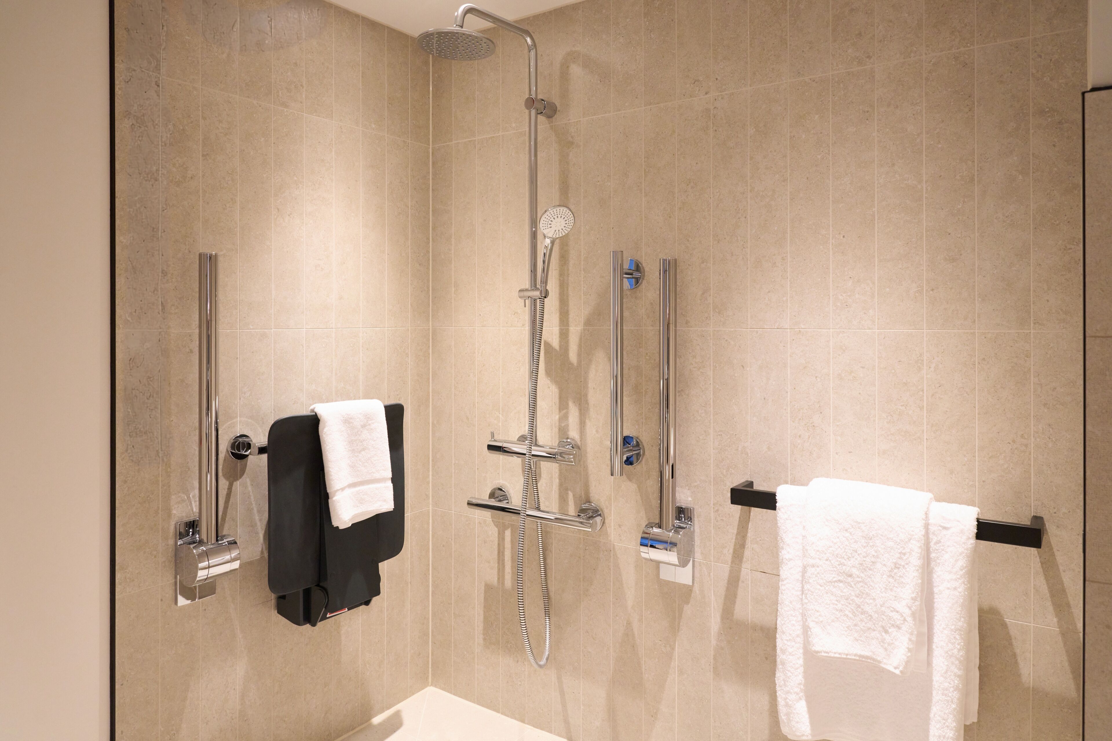 A modern bathroom with a shower, two towel racks, and a toilet paper holder.