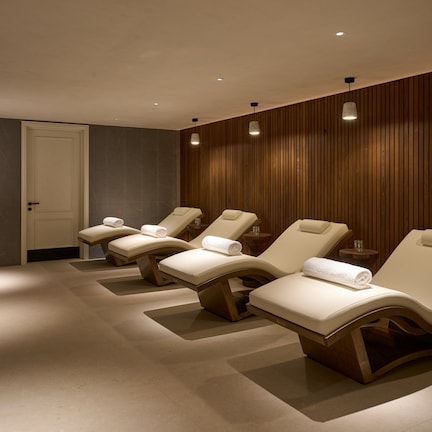 A spa room with four reclining chairs, a wooden wall, and a reception area with a fish tank.