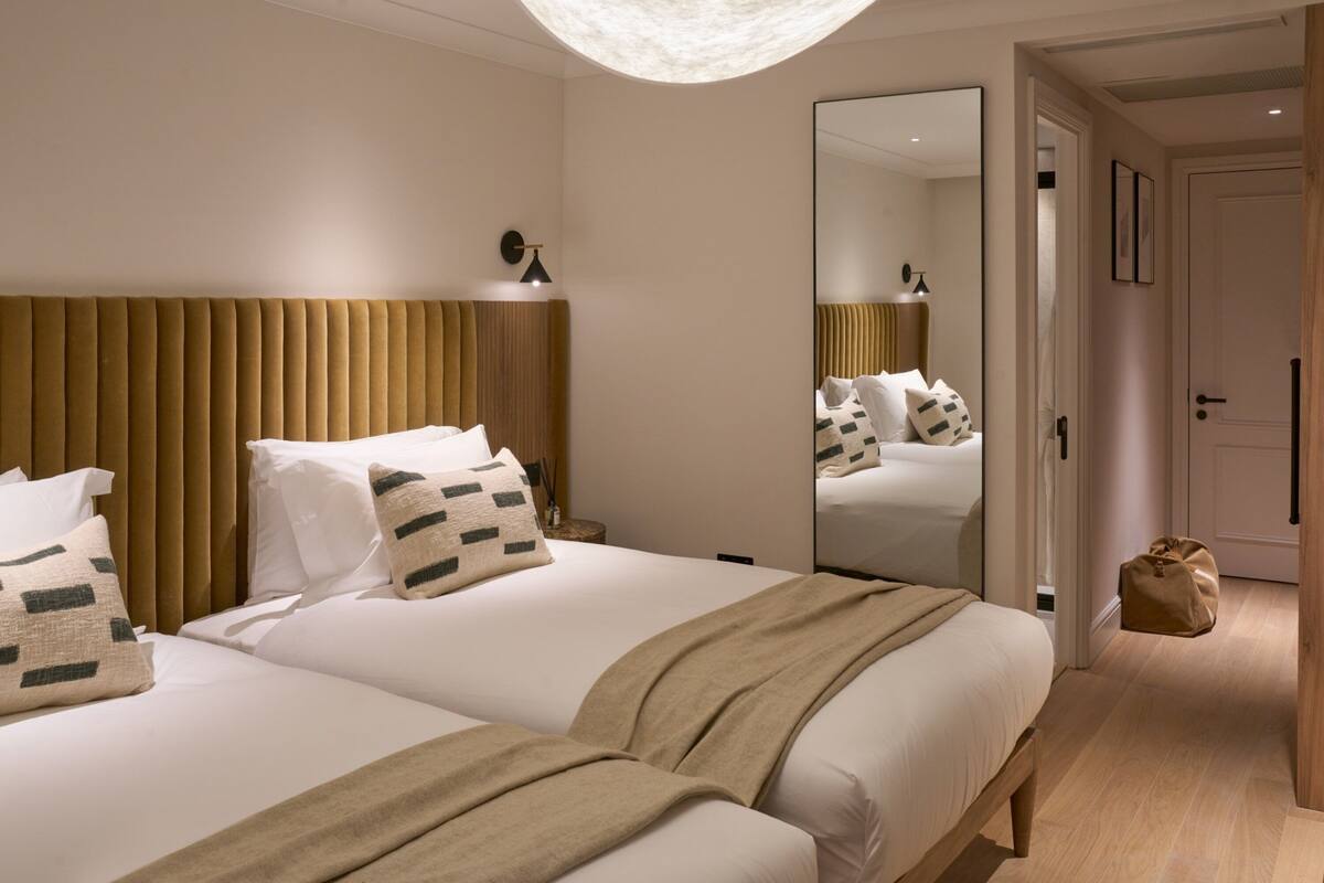 A hotel room with two beds, a large mirror, a wooden headboard, and a small bedside table with a lamp.