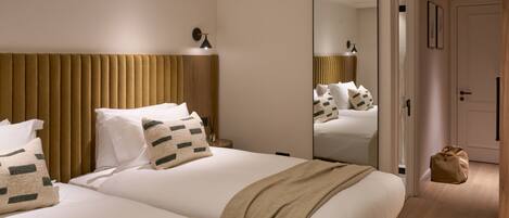 A hotel room with two beds, a large mirror, a wooden headboard, and a small bedside table with a lamp.