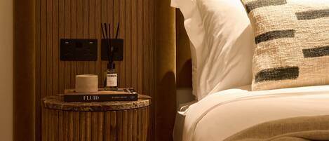 Ein Schlafzimmer mit einem Holz-Kopfteil, einem Nachttisch mit einer Flasche und einer Fernbedienung sowie einem Bett mit einer beige farbenen Decke und Kissen.