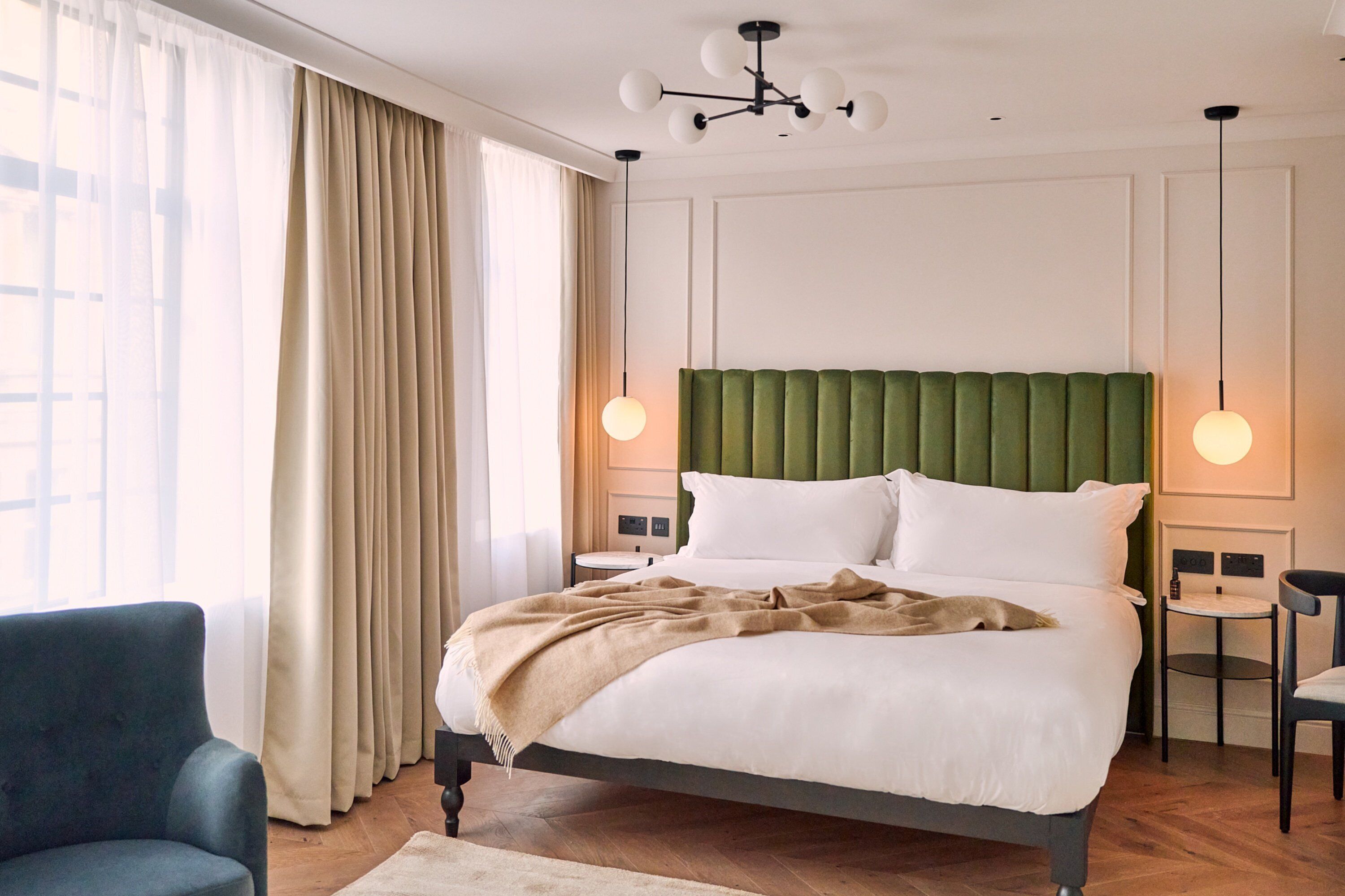 Een keurig opgemaakt slaapkamer met een groot bed, een stoel, een klein tafeltje en een kroonluchter.