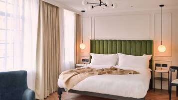 Een keurig opgemaakt slaapkamer met een groot bed, een stoel, een klein tafeltje en een kroonluchter.