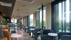 A modern cafe with a long counter, multiple seating areas, and large windows offering views of the city.