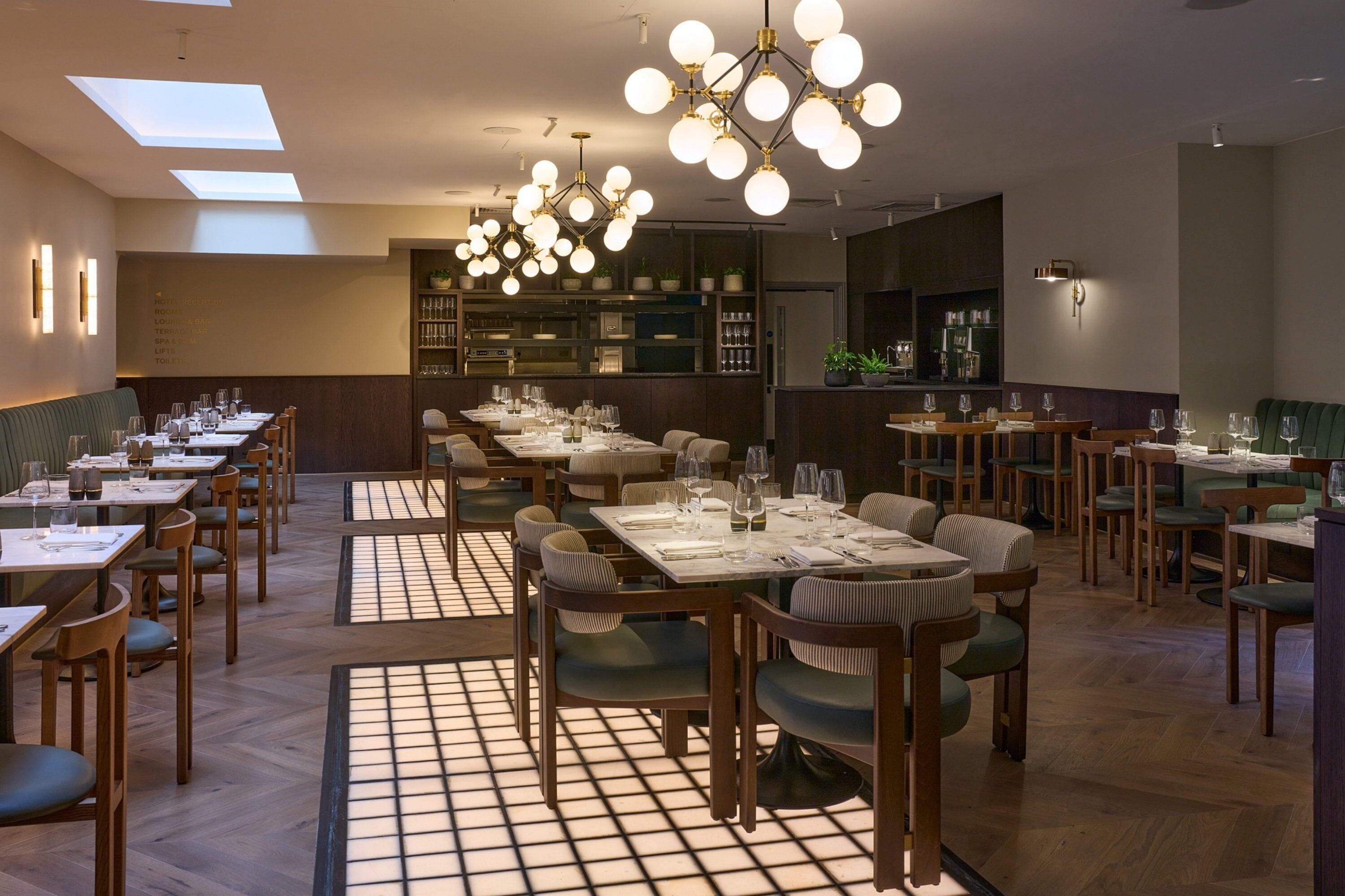 A restaurant with multiple dining tables and chairs, a bar area, and a kitchen in the background.