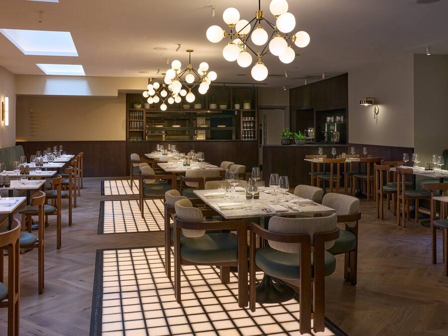 A restaurant with multiple dining tables and chairs, a bar area, and a kitchen in the background.