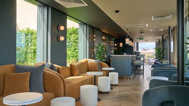 A modern hotel lobby with a sofa, round tables, and a bar area.
