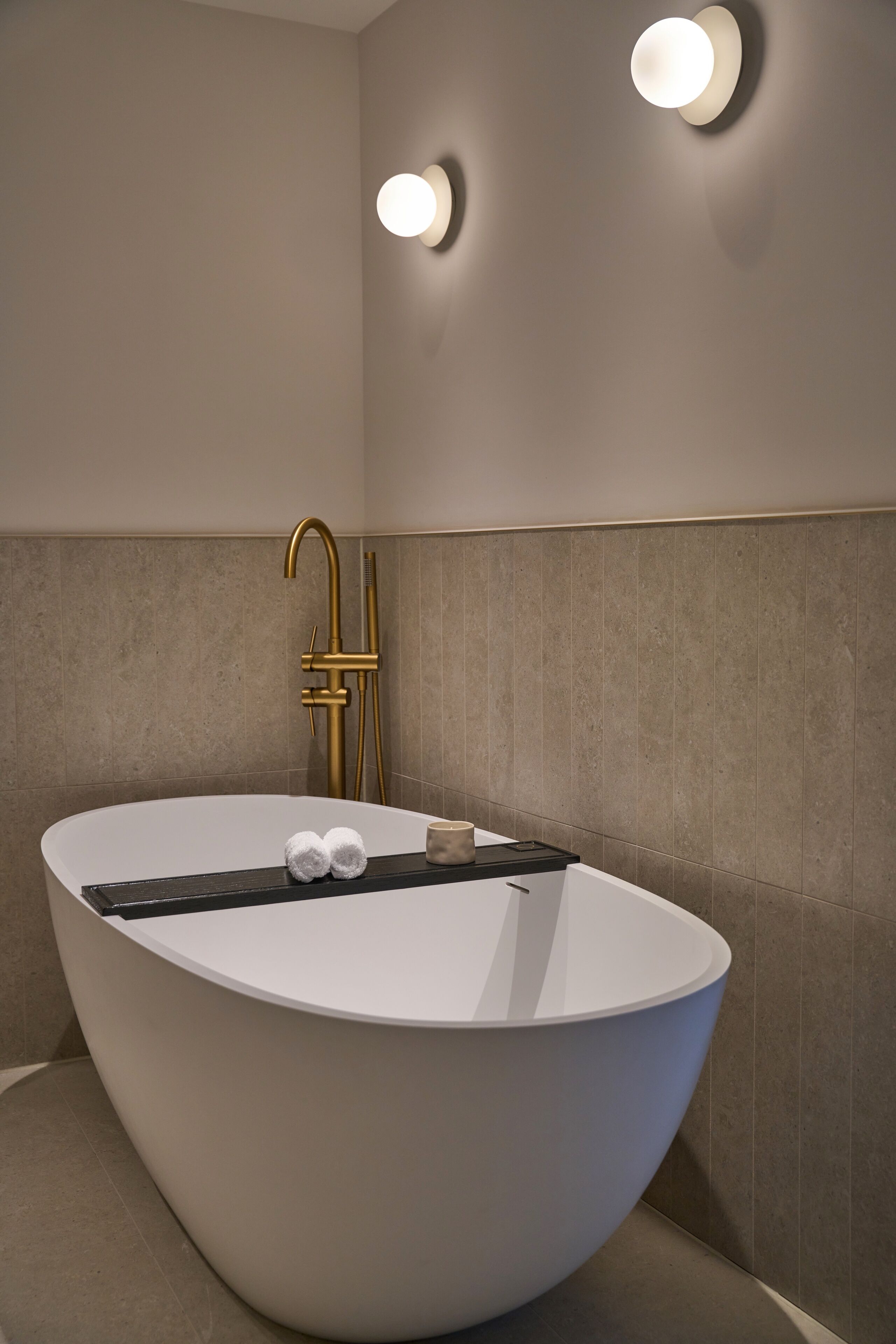 A modern bathroom with a freestanding bathtub, a gold faucet, and two wall-mounted lights.