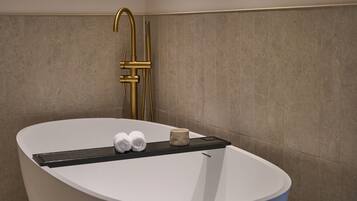 A modern bathroom with a freestanding bathtub, a gold faucet, and two wall-mounted lights.