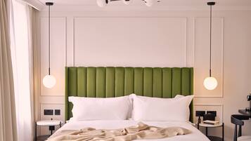 A neatly made bed with a green upholstered headboard, two bedside tables with lamps, and a view of the window with curtains.