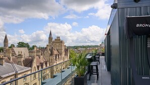 A rooftop terrace with a view of historic buildings, a railing, and a sign that reads "BROMIC".