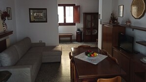 A living room with a sofa, a dining table with chairs, a TV, and a cabinet. - Annalú Holiday House (I.U.N. R5074) (Orosei)
