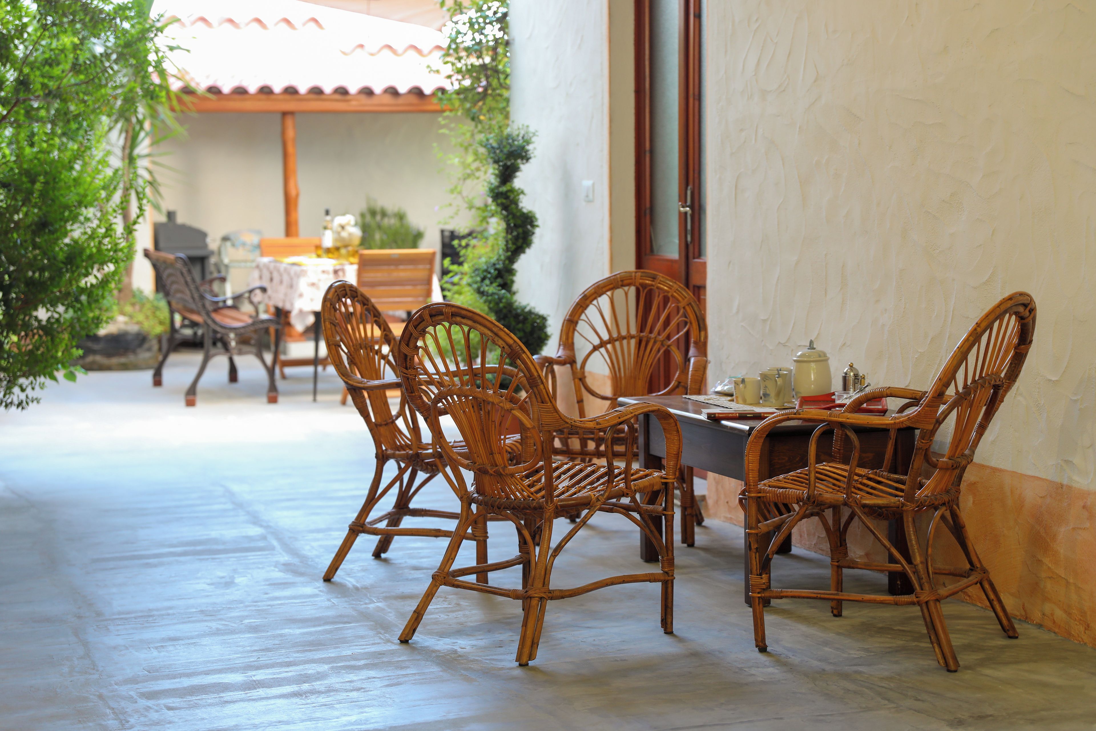 A dining area with wicker chairs and a table, a tiled floor, and a view of a building with a tiled roof.