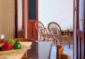 Un coin repas avec des chaises en osier et une table, une porte en bois et un mur blanc en arrière-plan.