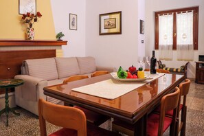 Un coin repas avec une table en bois, des chaises, un vase rempli de fleurs et une bouteille de vin.