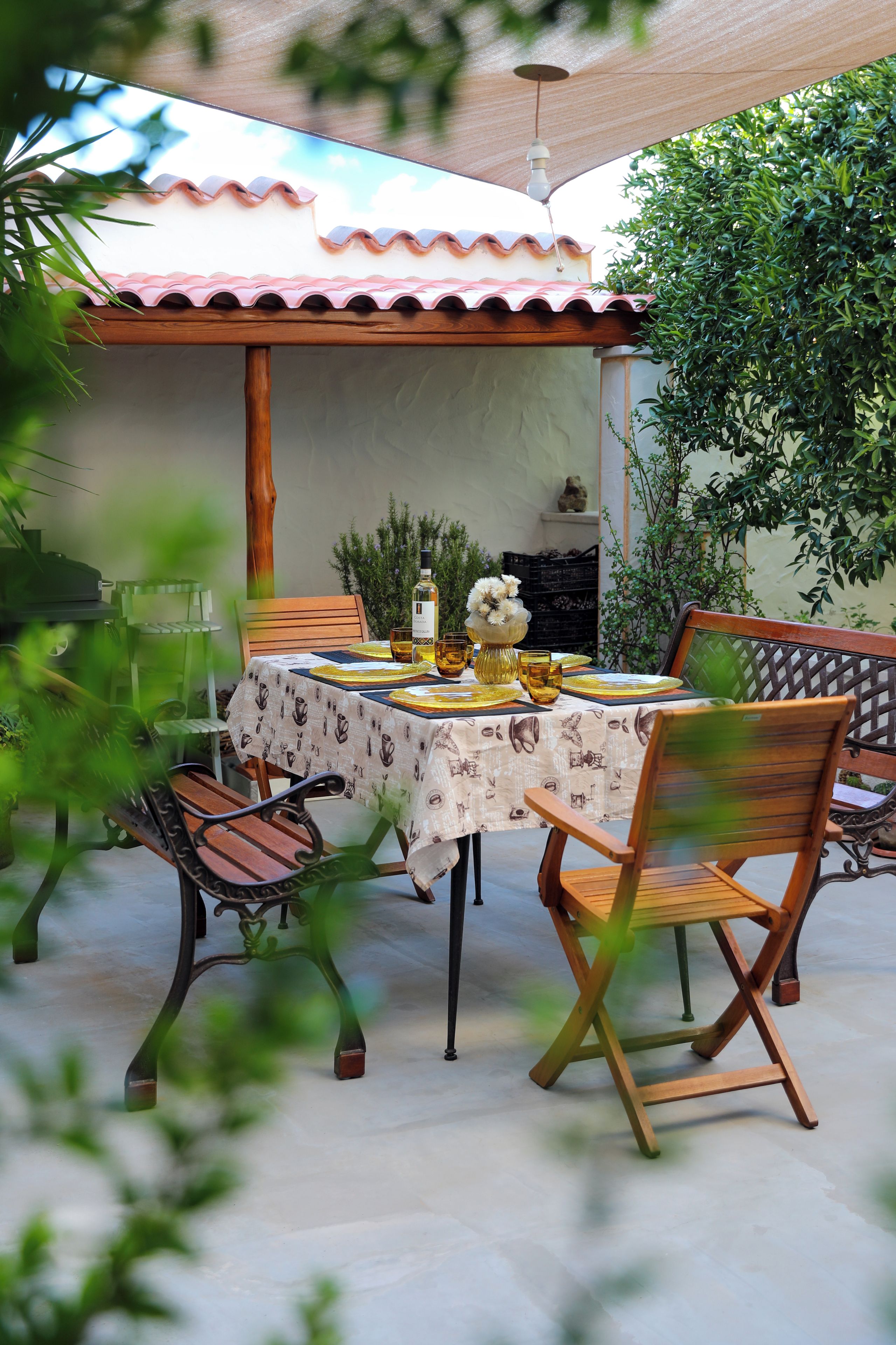 An outdoor patio with a table set for dining, surrounded by chairs and a decorative umbrella.