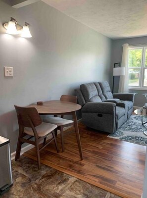 A dining area with a round table and chairs, a gray sofa, and a rug.