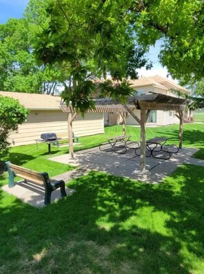 Un espace aménagé en parc avec une pergola en bois, des tables de pique-nique et un banc.